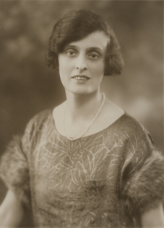 A photo of E. M. Delafield. She is wearing a pearl necklace and a dress with fur around its short sleeves.
