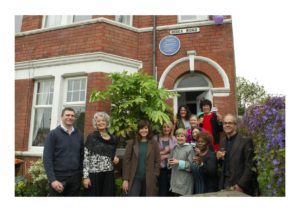 Group of people standing outside a house, with a circular blue plaque above the front door.